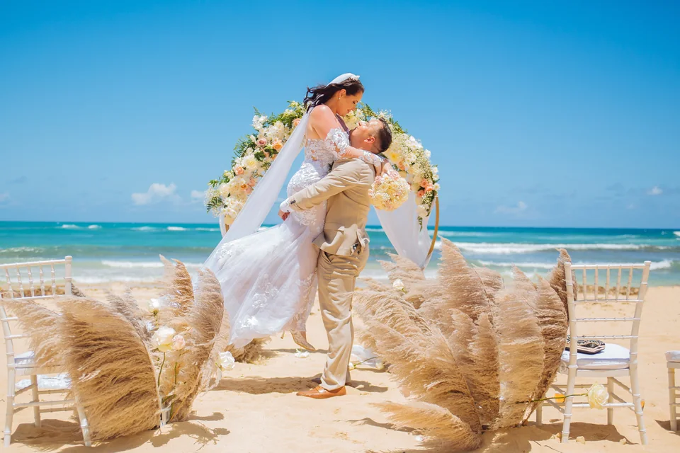 Pareja de recién casados celebrando bajo un arco floral con pampas en una playa de Punta Cana