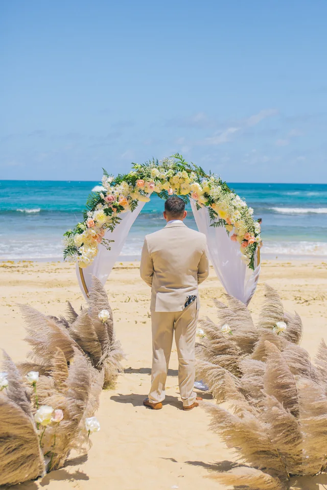 Novio esperando en un pasillo de ceremonia con pampas frente al mar en Punta Cana