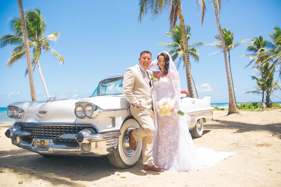 Pareja de elopement junto a un auto clásico blanco en una playa con palmeras de Punta Cana