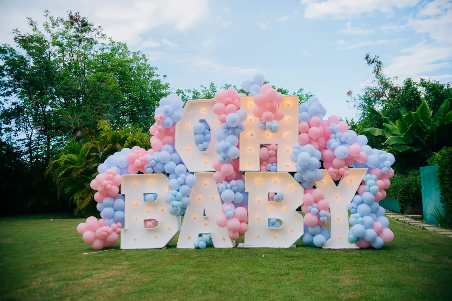Oh Baby letters and pastel balloons in a garden reveal setup